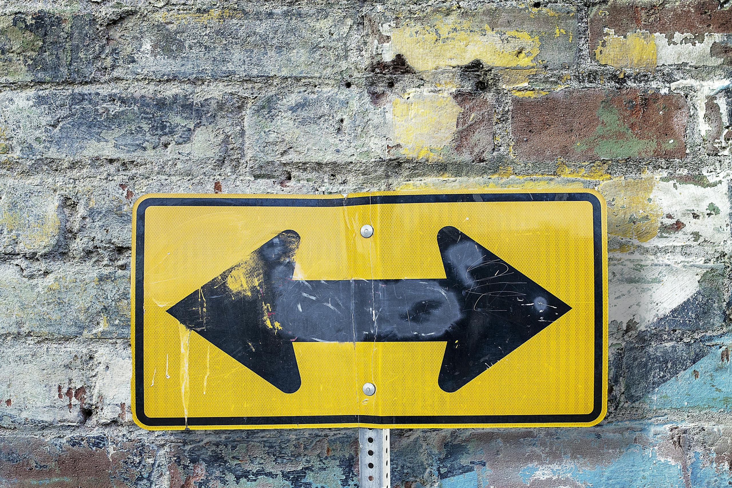Weathered yellow two-way street sign on a textured rustic brick wall. Urban art style.